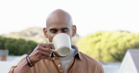 Mature man sipping coffee from ribbed ceramic mug on rooftop during soft morning light