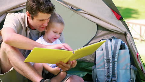 Father and Son Reading Together at Campsite in Front of Tent
