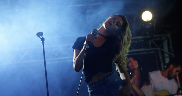 A young Caucasian woman performs passionately on stage as a singer, with copy space. She is accompanied by musicians, creating a lively concert atmosphere.