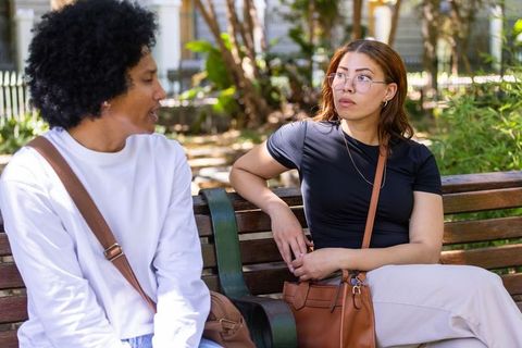 African american friends sitting on park bench talking, casual outdoor conversation