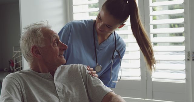 Image captures a nurse providing care and companionship to a senior patient in a healthcare facility. The nurse, dressed in medical scrubs and a stethoscope, is gently holding the elderly man's shoulder. Suitable for healthcare, eldercare services, nursing homes, medical blogs, and caregiving topics.