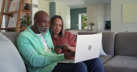 Mature couple using laptop and credit card on sofa for online banking and home shopping