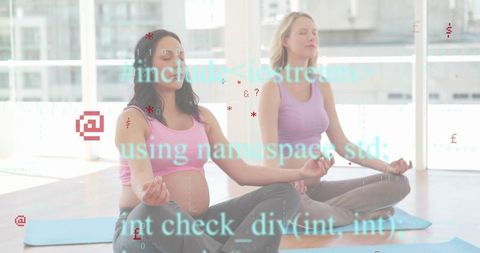 Pregnant woman and partner meditating on yoga mats in sunlit studio with code overlay