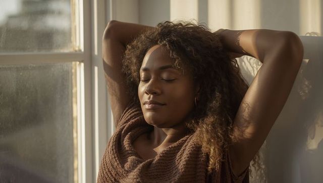 Serene woman relaxing by sunlit window at home, peaceful moment of natural calm