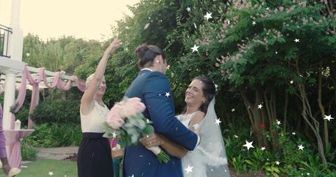 Bride and partner embracing in garden wedding with veil and pink rose bouquet