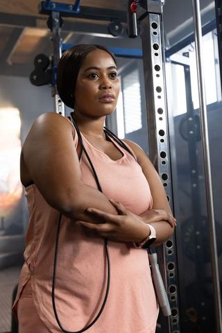 African american woman standing by squat rack wearing pink tank top with jump rope focused