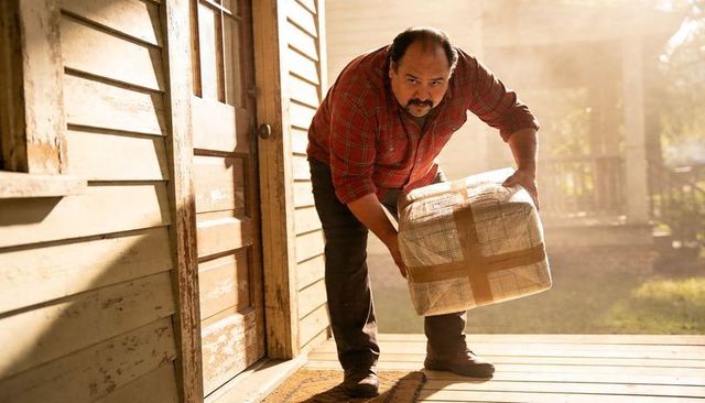 Man lifting large taped parcel on sunlit rustic porch during golden hour delivery concept