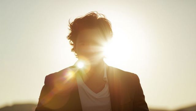 Man standing backlit at golden hour with lens flare, blazer and v-neck