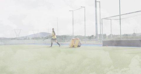 Field hockey action with goalkeeper diving and player in yellow bib on synthetic turf