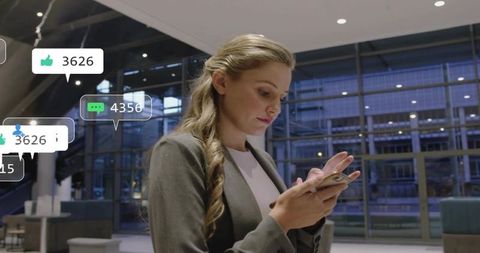 Businesswoman using smartphone in modern glass atrium with floating social notifications