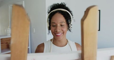 African american woman painting at easel wearing headphones smiling in bright home studio