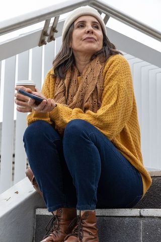 Middle-aged woman relaxing on urban stairway sipping coffee and checking smartphone screen
