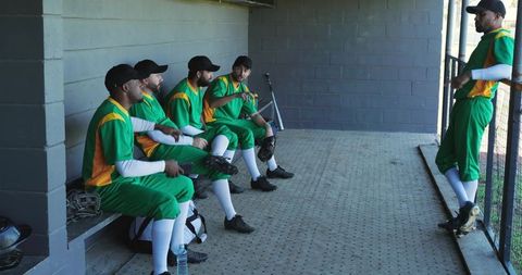 Multicultural baseball team resting in dugout wearing green and yellow uniforms