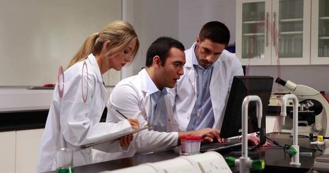 Collaborative laboratory team reviewing data on computer and taking notes at modern research bench