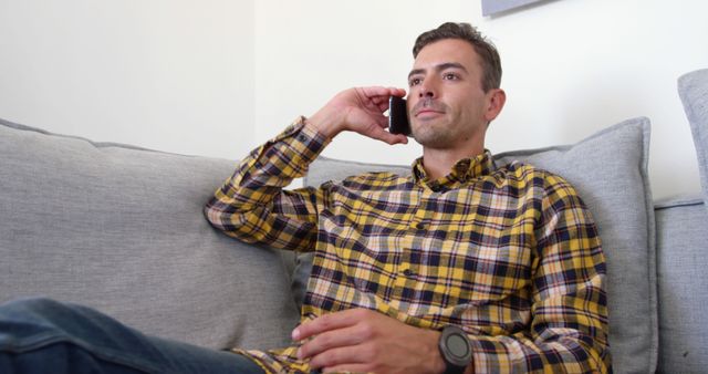 Man having a phone conversation while sitting on couch at home. Great for use in articles and advertisements about communication, technology, mobile devices, and lifestyle.