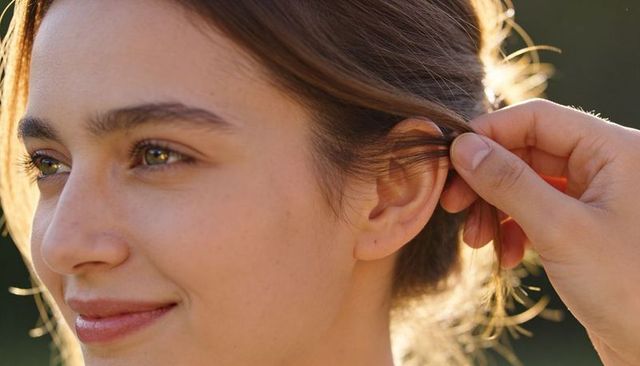 Smiling young woman tucking hair behind ear in golden hour portrait with freckles and hand