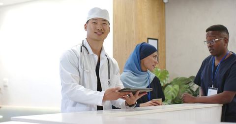 Multicultural medical team presenting tablet at clinic reception, collaborating on patient care