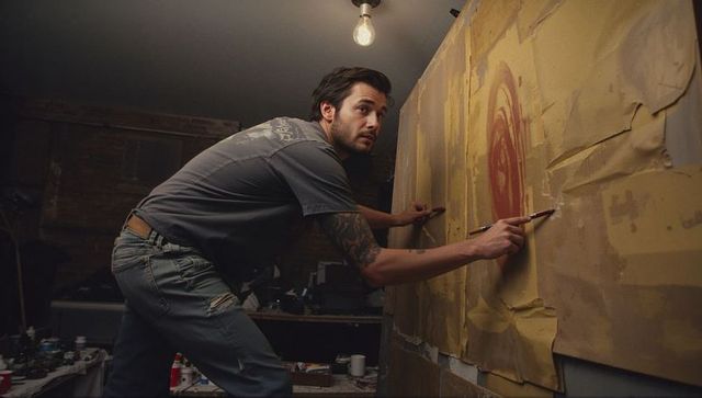 Male artist in basement studio creating large canvas mural