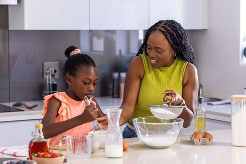 African american mother teaching daughter baking at modern sunlit kitchen island