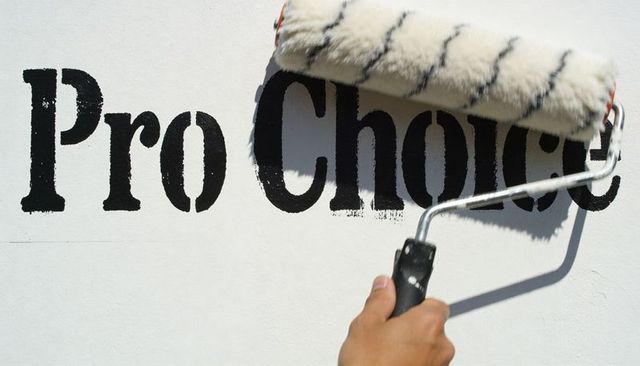 Overpainting Pro-Choice Stencil with Paint Roller, Creating Censorship Metaphor on Wall