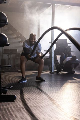 African american man powering battle ropes in industrial gym training with intense backlit