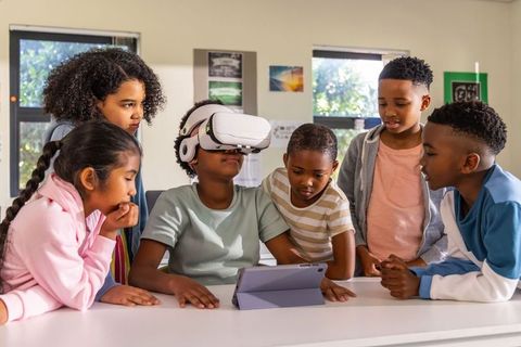 School children exploring virtual reality with tablet in classroom for collaborative stem
