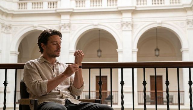 Man adjusting wristwatch on balcony in neoclassical gallery with arched courtyard