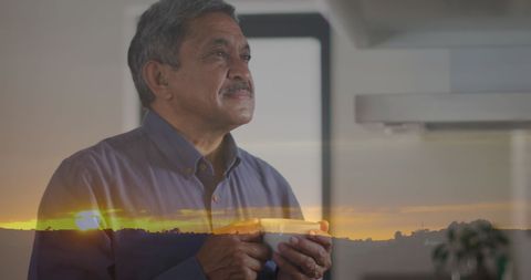 a senior man is holding a cup, enjoying the serene moment with a digital double exposure of a scenic sunrise. the image conveys themes of peace, mindfulness, and appreciation of nature. suitable for use in wellness and serenity advertising campaigns, healthcare newsletters, or lifestyle articles centered around tranquility and positive aging.