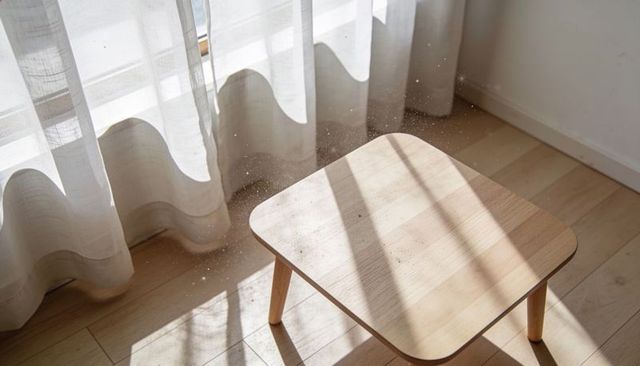 Sunlit minimal wooden side table with dust particles sparkling through sheer curtains