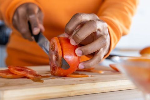 African american hands slicing ripe tomato with chef knife on wooden cutting board