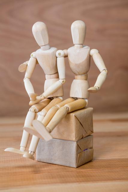 Wooden figurine couple sitting closely on a box, symbolizing love and companionship. Ideal for use in relationship blogs, art projects, conceptual designs, and educational materials about human connections.