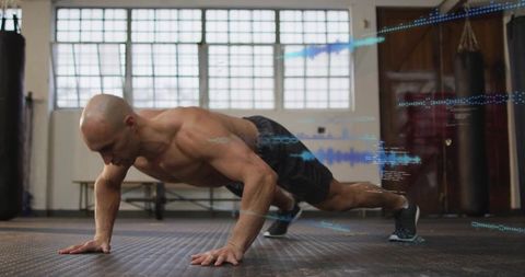 Shirtless athletic man doing pushup in boxing gym with blue digital fitness overlays