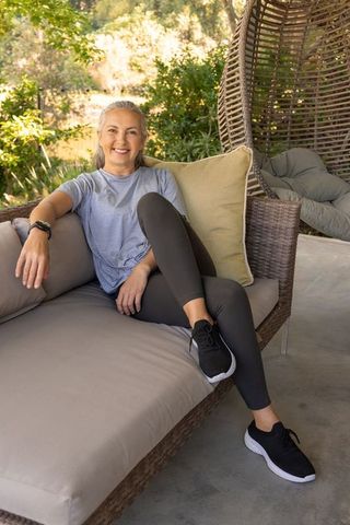 Senior woman relaxing on wicker sofa in sunlit patio wearing activewear and smartwatch