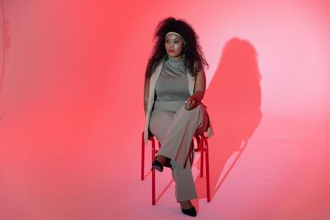 Mid-adult african american woman sitting on red chair with pink gradient studio lighting