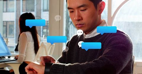 Asian man checking smartwatch while receiving chat notifications in modern open-plan office