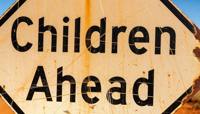 Weathered children ahead warning sign showing rusted scratches and patina in desert