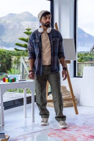 Young artist standing in sunlit studio with easel, headphones and mountain view