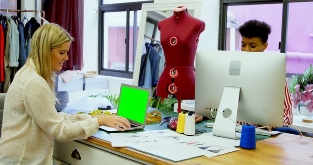 Fashion designers collaborating over a computer and sewing dummy in an office. Useful for illustrating creative workspaces, teamwork in the fashion industry, or showcasing the design process in textiles and clothing businesses.