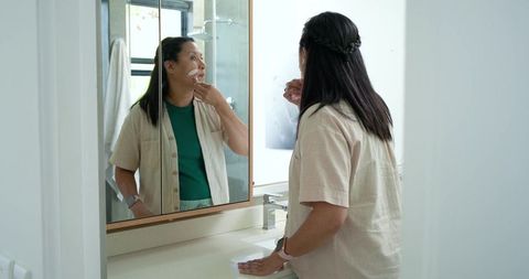 Middle-aged african american woman applying facial cleanser at bathroom vanity mirror