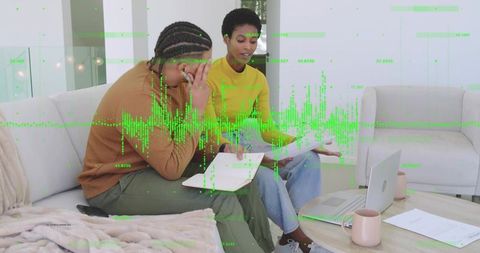 Collaborating on financial analysis with laptop and green waveform overlay at home workspace