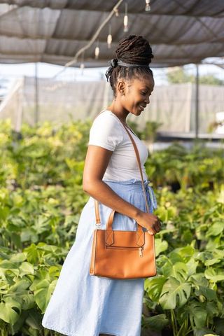 African american woman standing in greenhouse among monstera plants carrying brown handbag