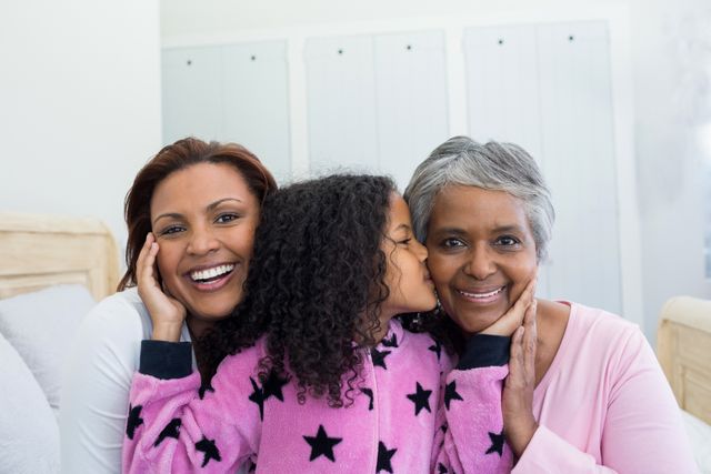 Three generations of women, including a grandmother, mother, and daughter, sharing a loving moment at home. The young girl is kissing her grandmother on the cheek while the mother smiles warmly. Ideal for use in family-oriented advertisements, articles on family bonding, and promotions for home and lifestyle products.