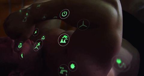 Shirtless man lying shielding face with forearm amid green holographic tech icons