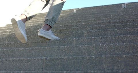 Ascending concrete steps wearing white sneakers and cuffed pants, urban motion and texture