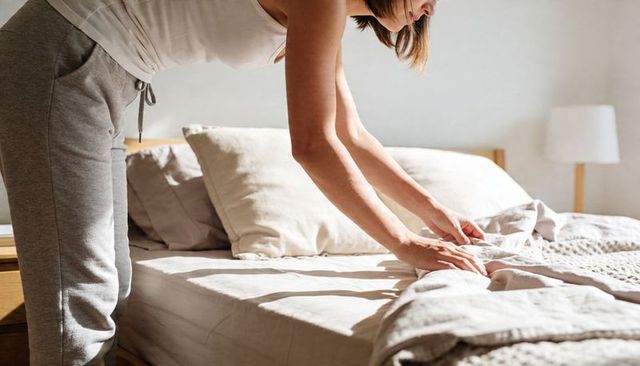 Woman smoothing linen duvet on sunlit minimalist bed morning routine cozy neutral textured linens