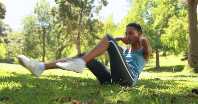Active woman performing bicycle crunches in a serene park setting on a sunny day. Ideal for promoting outdoor exercise, fitness regimes, and healthy living campaigns. Can be used in fitness magazines, workout guides, and wellness blogs.