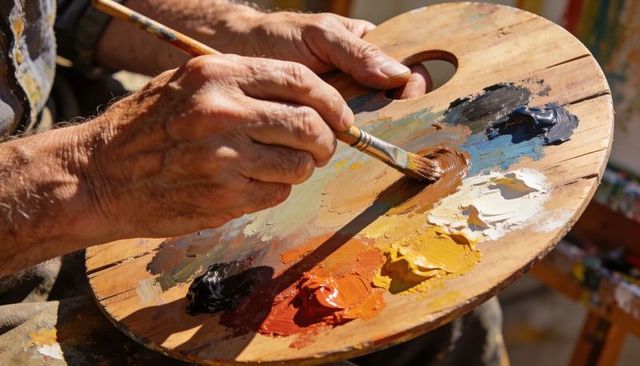 Artist mixing oil paints on wooden palette with brush and textured color swatches