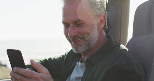 Senior man smiling while using smartphone in car on a sunny day - Download Free Stock Images Pikwizard.com