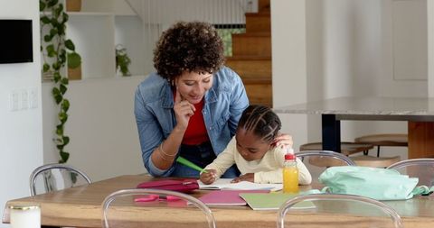 Mother Encouraging Daughter During Homeschool Writing Task at Wooden Table