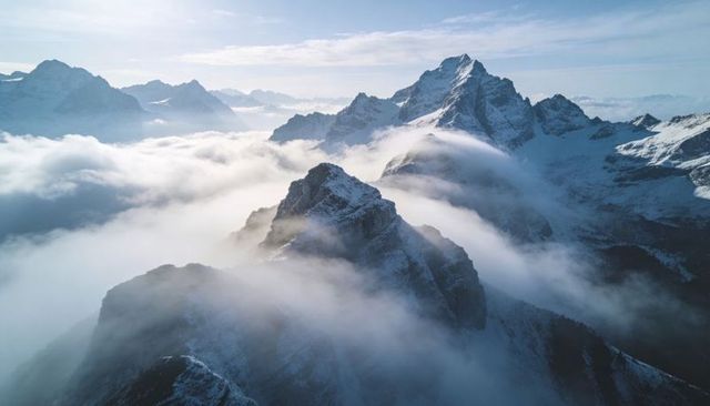 Snow-dusted ridge rising above alpine cloud inversion with sunlit jagged peaks